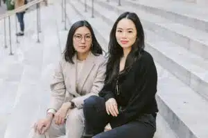 Florence Shin and Athena Wang of Covry sitting on gray steps wearing black and gray outfits.